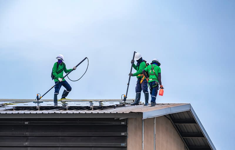 Group of professional cleaning service workers clean the solar panels on industrial building roof